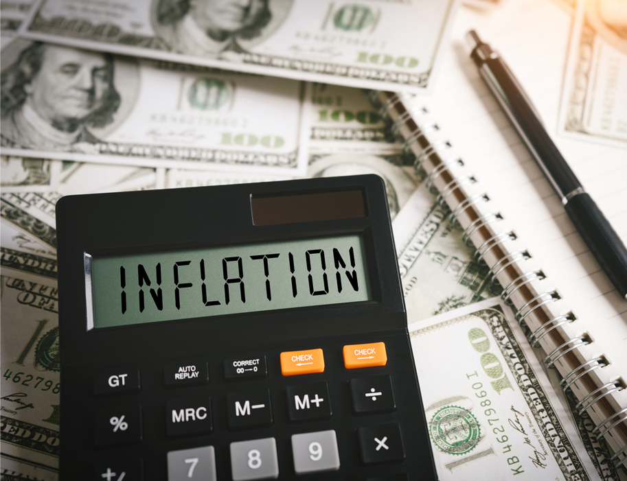 Calculator displaying the word inflation, sitting on 100 dollar bills next to a notepad and pen